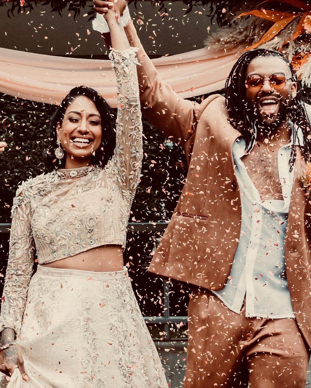 130539 oritse and his wife kazza holding hands in the air in neutral coloured wedding outfits as confetti is thrown on them at their celebrity wedding