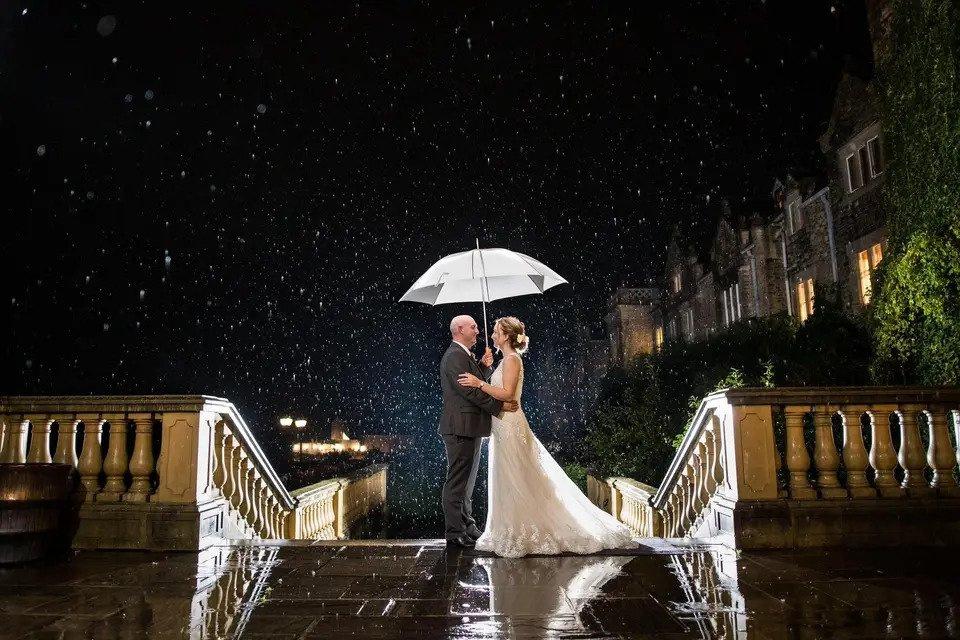 Bride and groom stand under an umbrella on the pavilion in the dark