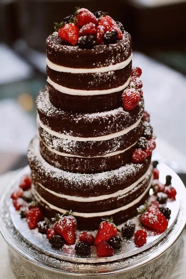 Dark brown naked cake dusted with icing sugar and topped with berries