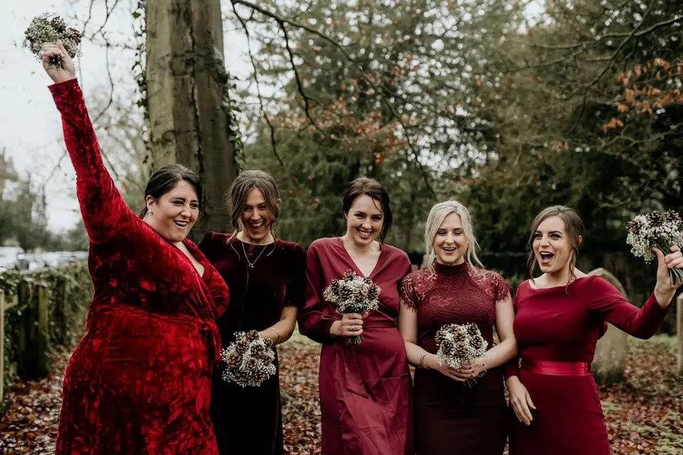 Five bridesmaids posing for a bridesmaid picture laughing together wearing mismatched red bridesmaid dresses