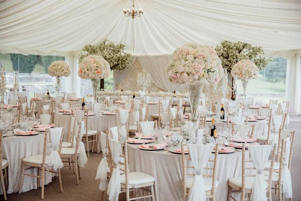 marquee venue with white round tables, white chaivari chairs with sashes, white floral centrepieces, floor-to-ceiling windows and a chandelier