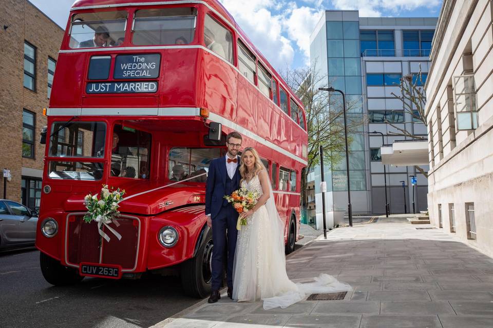 The bride and groom pose in front of a London bus