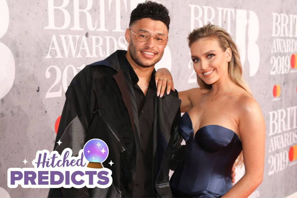 Perrie Edwards on the red carpet for the Brit Awards 2019 smiling in a navy, strapless cocktail dress next to her fiance Alex Oxlade-Chamberlain, who is wearing a dark jacket and top