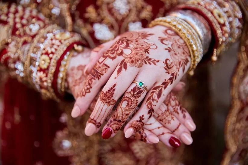 A close up photo of a bride's hand, showing her emerald wedding ring and intricate bridal mehendi