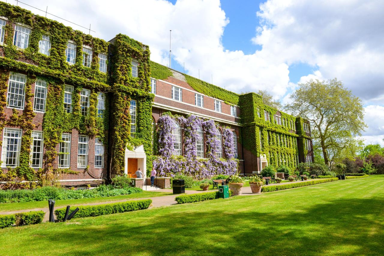 Exterior of an ivy and wisteria clad college building in formal gardens.