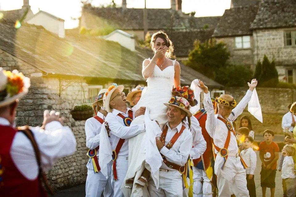 Surprised bride is lifted up by Morris dancers outdoors