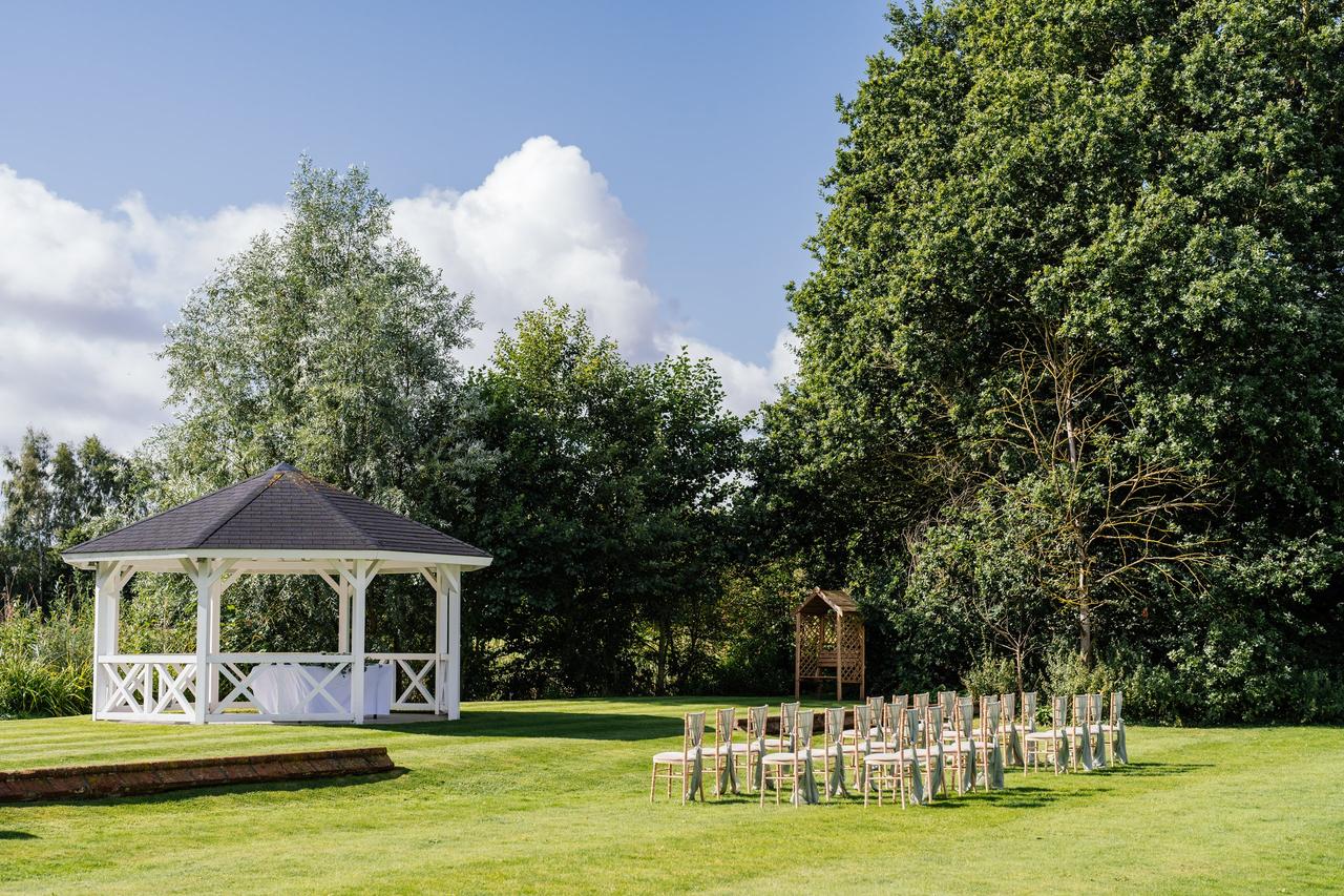 A manicured lawn with a pagoda and chairs set up for a wedding ceremony.