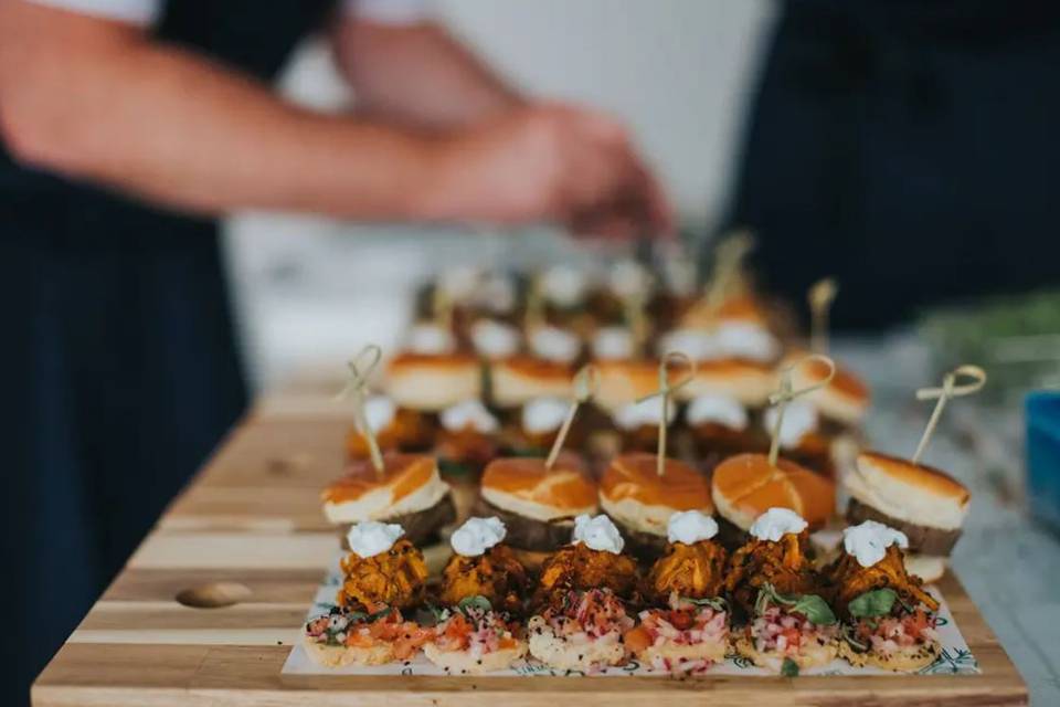 a wooden platter of sliders and unique wedding food ideas served as canapes on cocktail sticks
