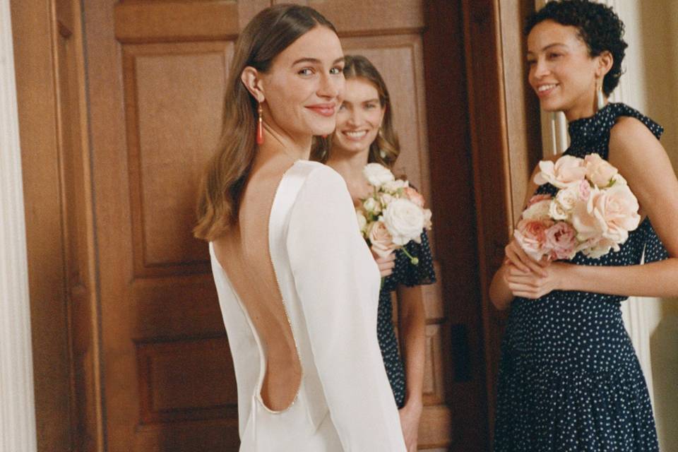 bride turning to face the camera wearing a low backed rixo wedding dress with two bridesmaids in polka dot dresses behind her