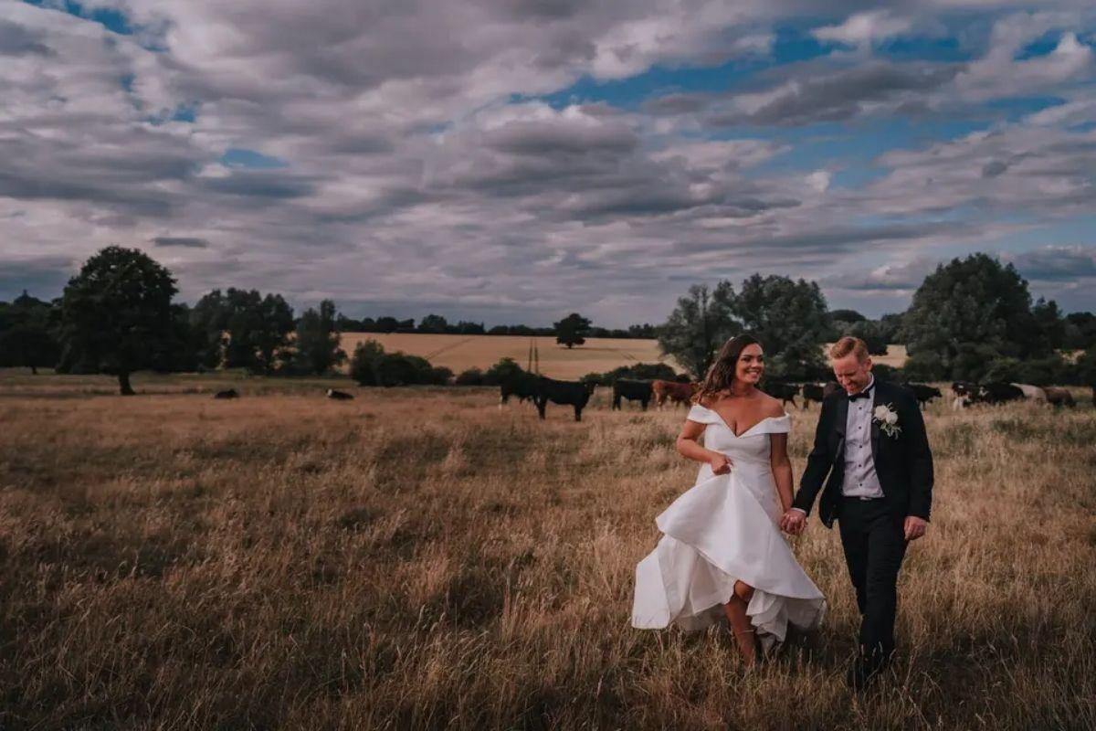 a bride and groom walking through a field of animals in traditional wedding attire