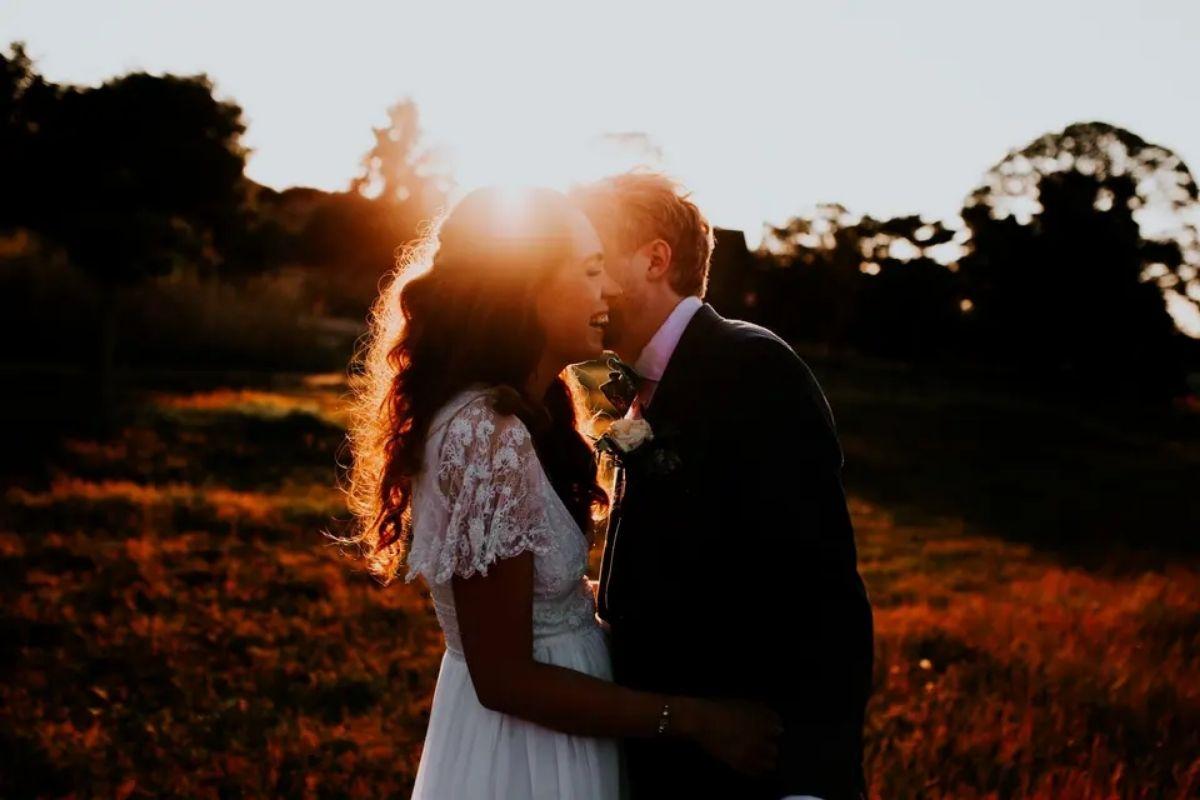 the sun shines brightly as a couple pose in the foreground and kiss one another