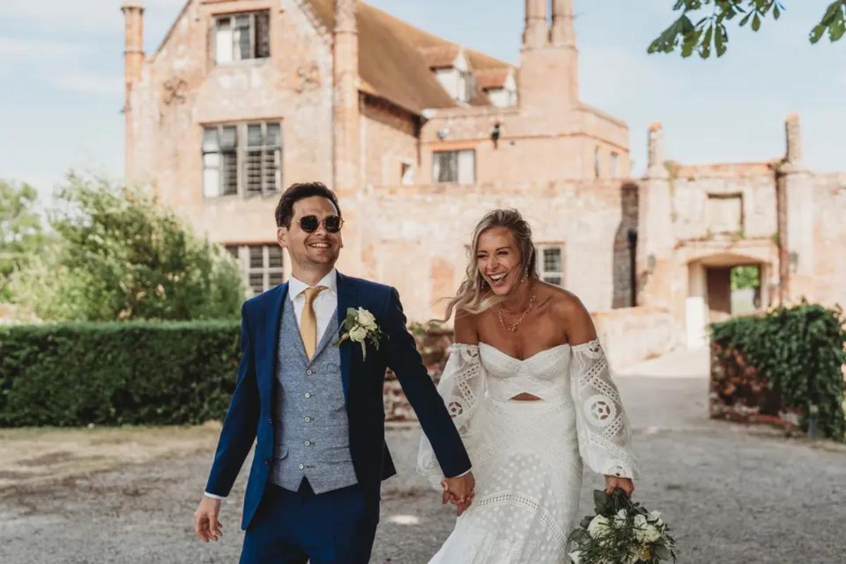 A bride and groom holding hands and laughing outside Suffolk wedding venue Crow's Hall