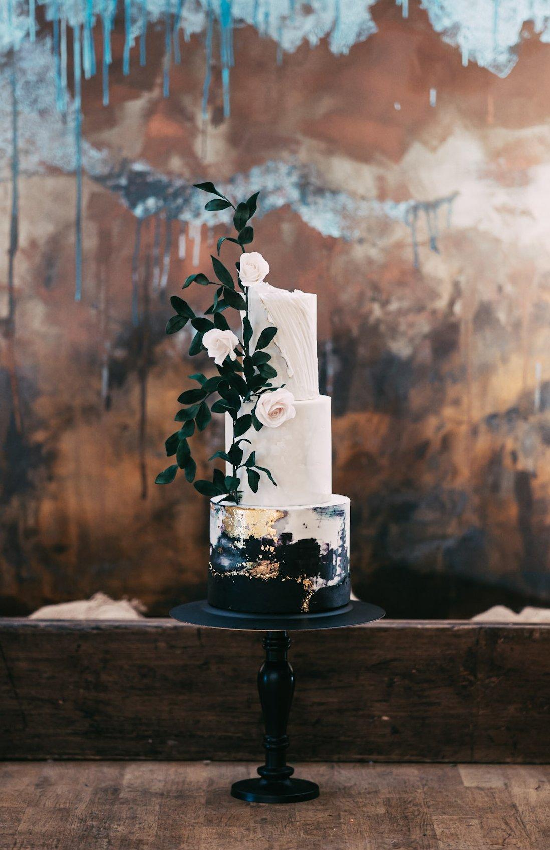 White wedding cake with pale pink sugar flowers, black icing on the bottom tier and gold leaf detailing