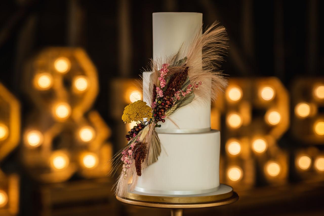 A simple white wedding cake with spray of dried flowers and berries on the front.