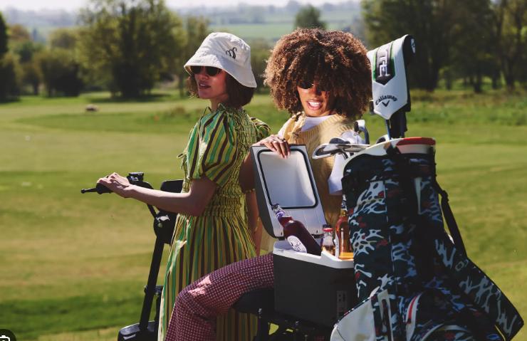 two women on a golf buggy heading out onto a golf course