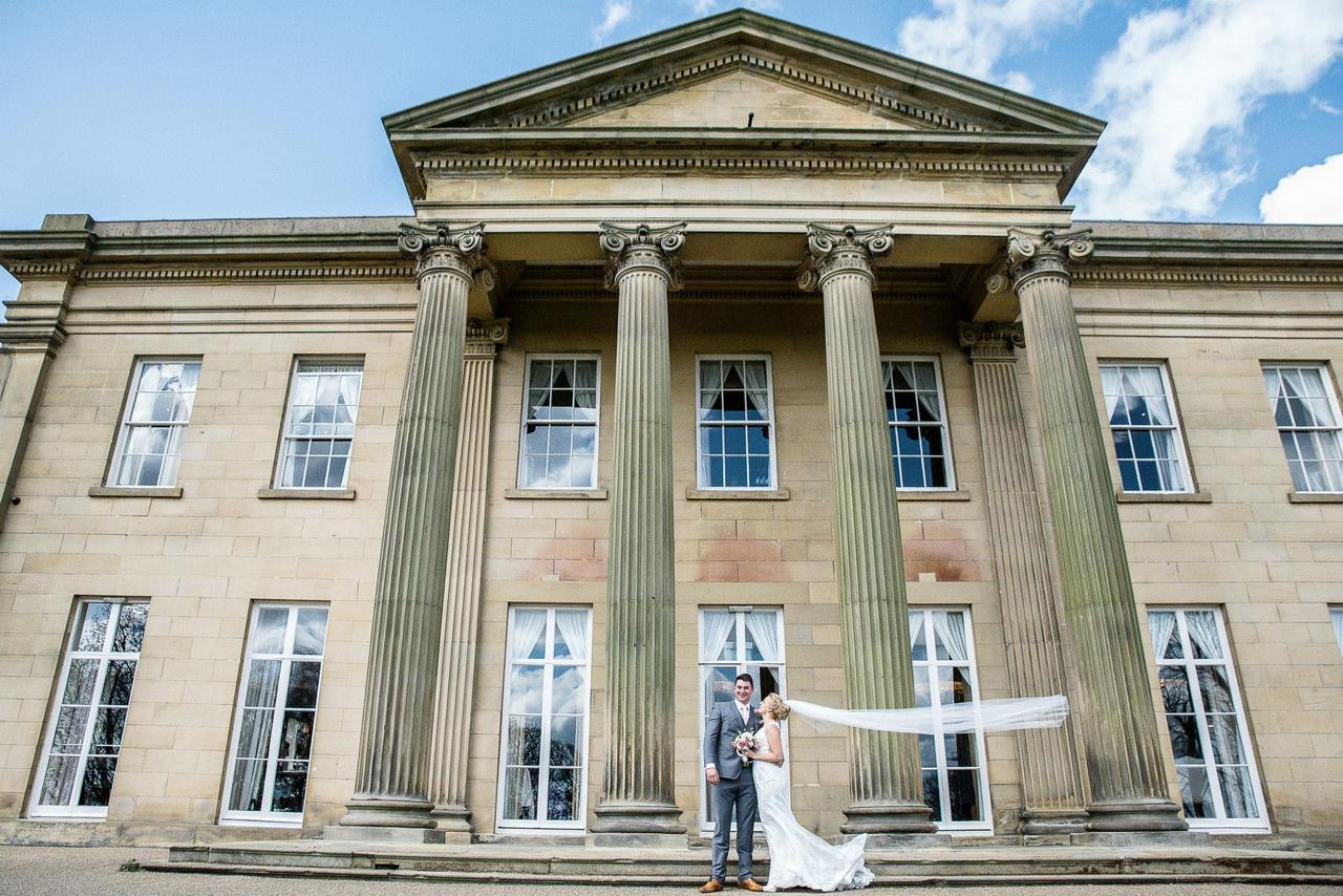 Exterior of a grand stately home wedding venue with tall columns and a couple in wedding attire