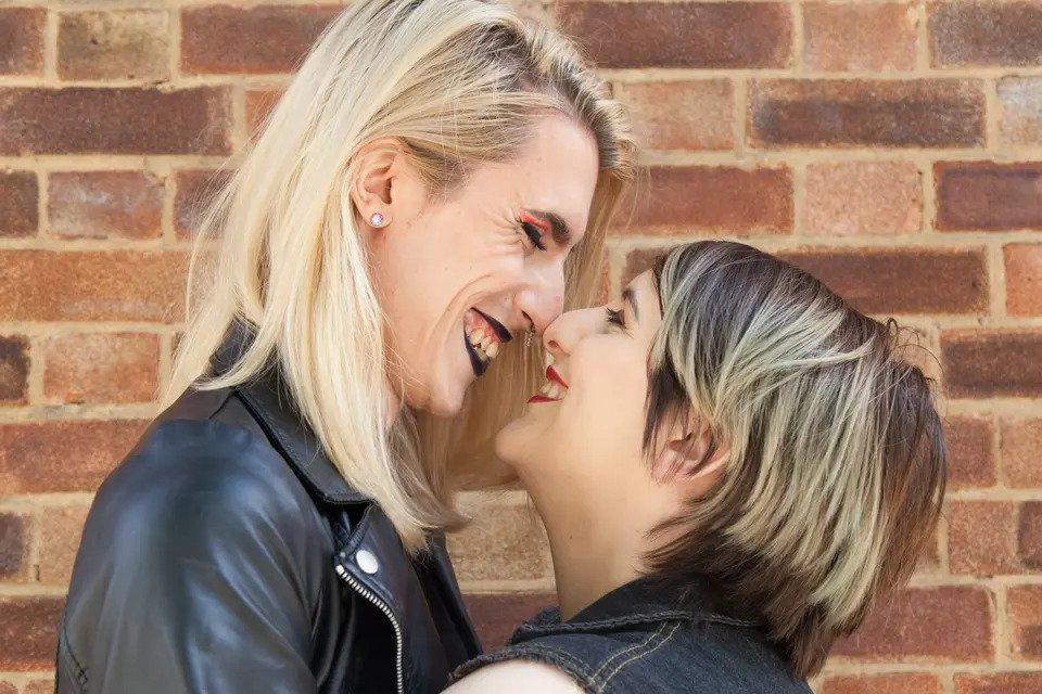 Close up shot of a couple leaning for a kiss and candidly laughing in front of a brick wall