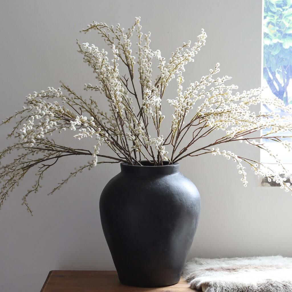 An arrangement of faux willow stems in a large grey vase.