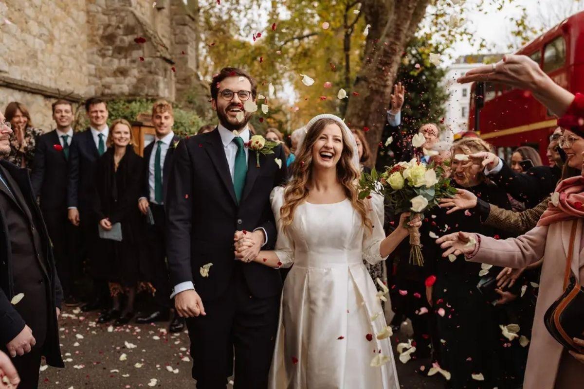 a bride and groom walk and smile as their guests shower them with beautiful confetti