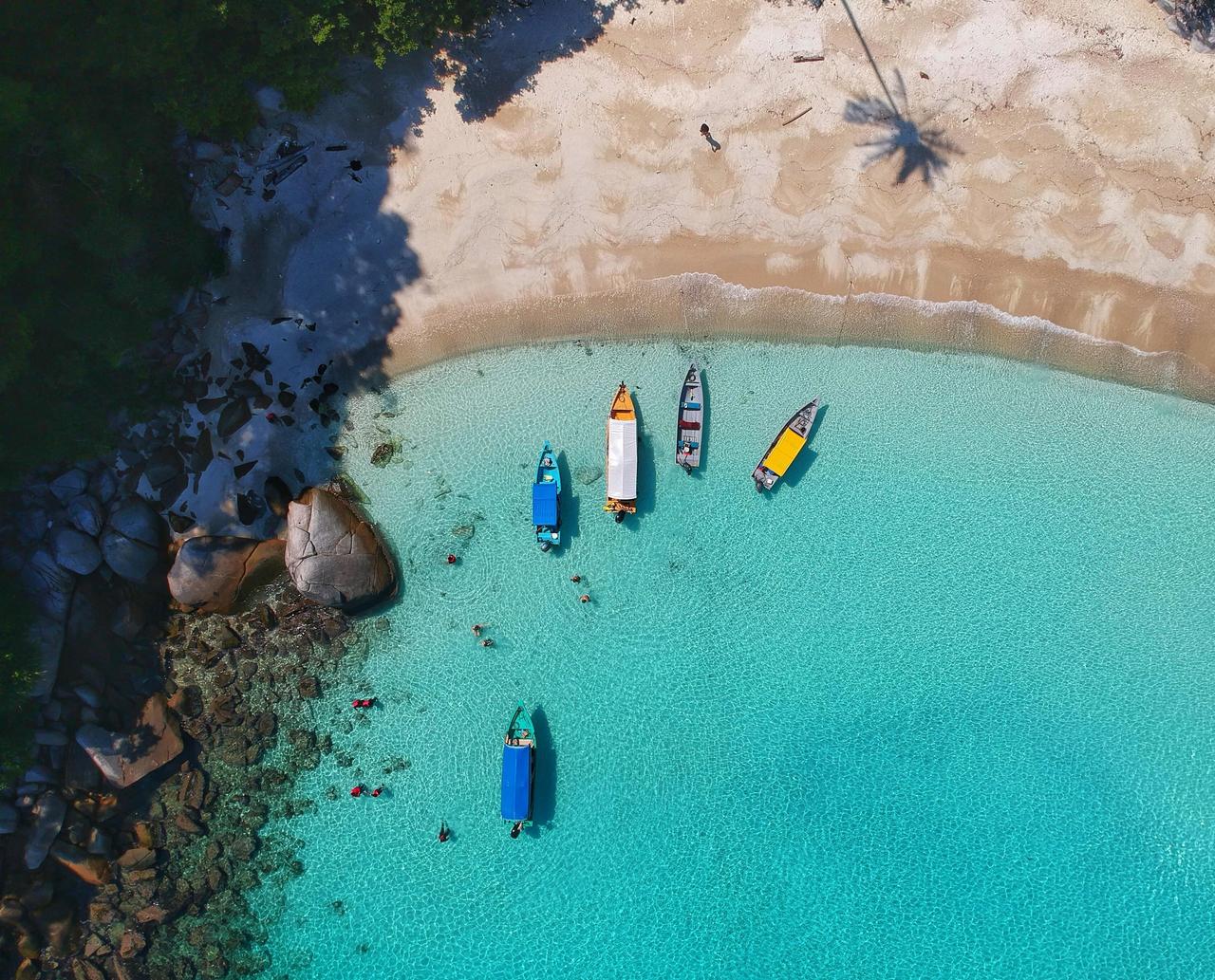 a picture of boats during a hoenymoon in may approaching a beach while sailing on clear turquoise waters