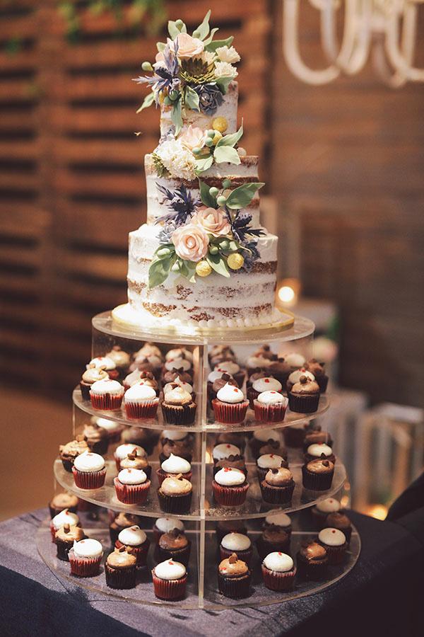 Three tiered semi naked rustic wedding cake with mini cupcake display