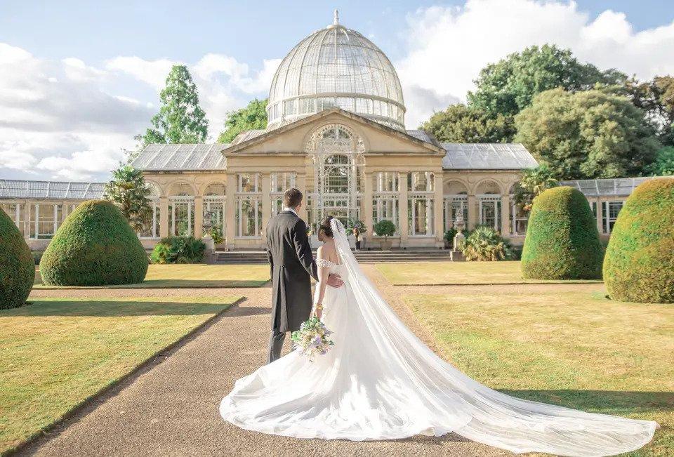 Bride and groom photographed from behind in front of a large greenhouse