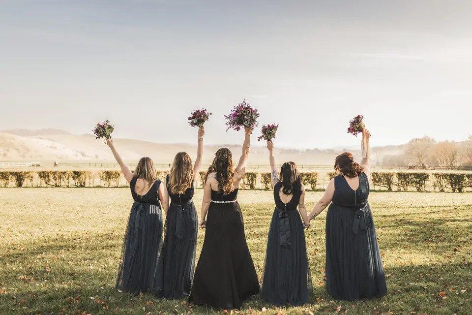 Photo of five bridesmaids taken from behind showing the backs of their dresses and hairstyles as they hold their bouquets up in the air