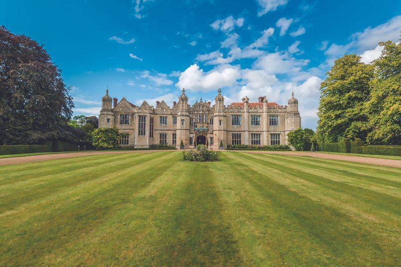 A large stately home wedding venue photographed face-on with a huge lawn in front of it and trees either side