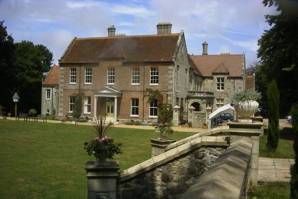 Red brick exterior of Landguard Manor taken from a stone wall behind a manicured green lawn