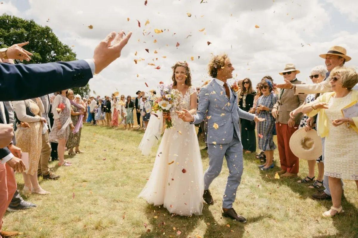 a couple walking out to see their guests as they throw confetti at a festival style outdoor summer wedding