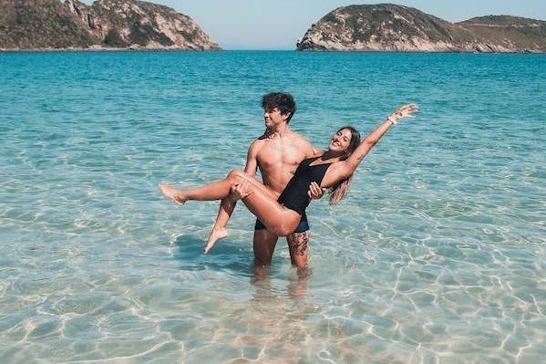 Couple posing in the sea on a beach on their honeymoon - the man is holding the woman in his arms as she poses with her arms extended