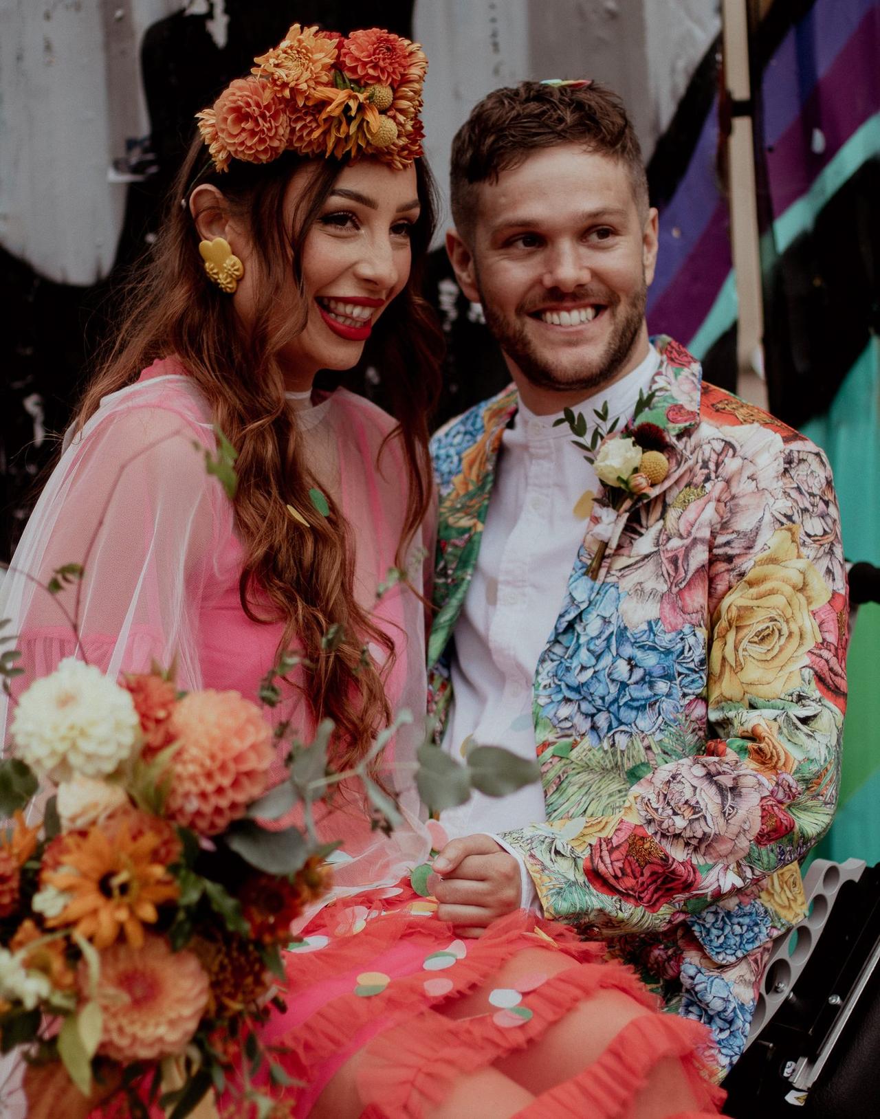 https://cdn0.hitched.co.uk/article/9769/original/1280/jpg/129679-couple-smiling-on-their-wedding-day-with-the-bride-sitting-on-her-grooms-lap-both-dressed-in-colourful-outfits-ellie-cooper-hitched.jpeg