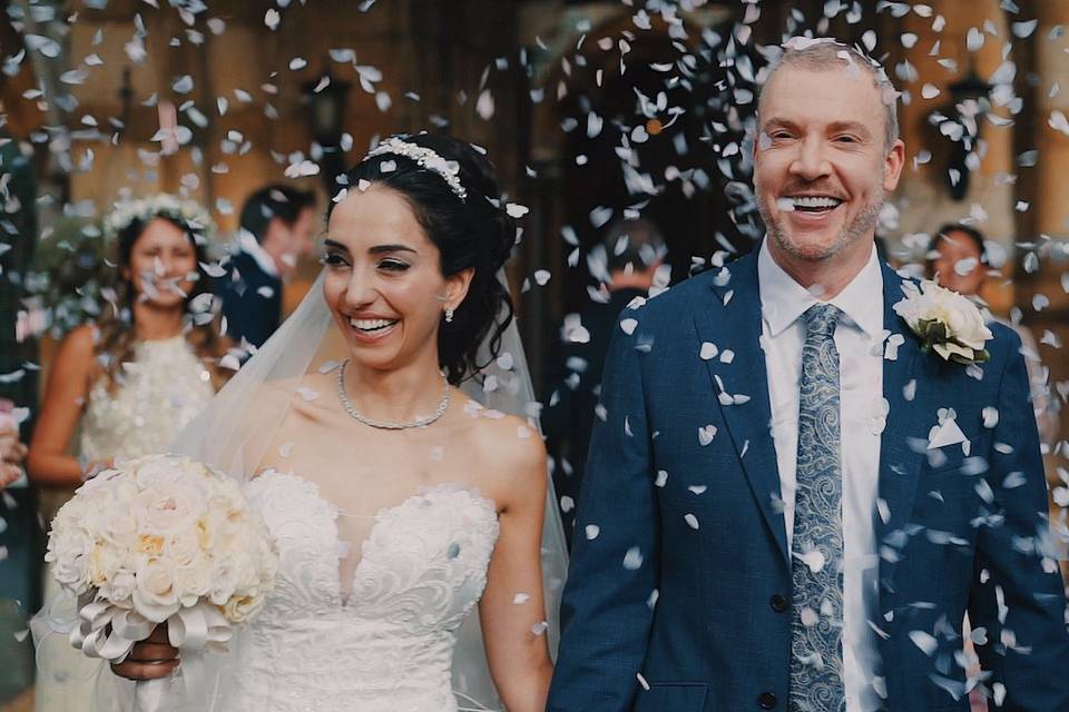 A married couple leave a church while their guests throw confetti