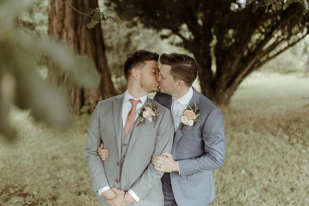 The grooms kiss under the shade of a tree