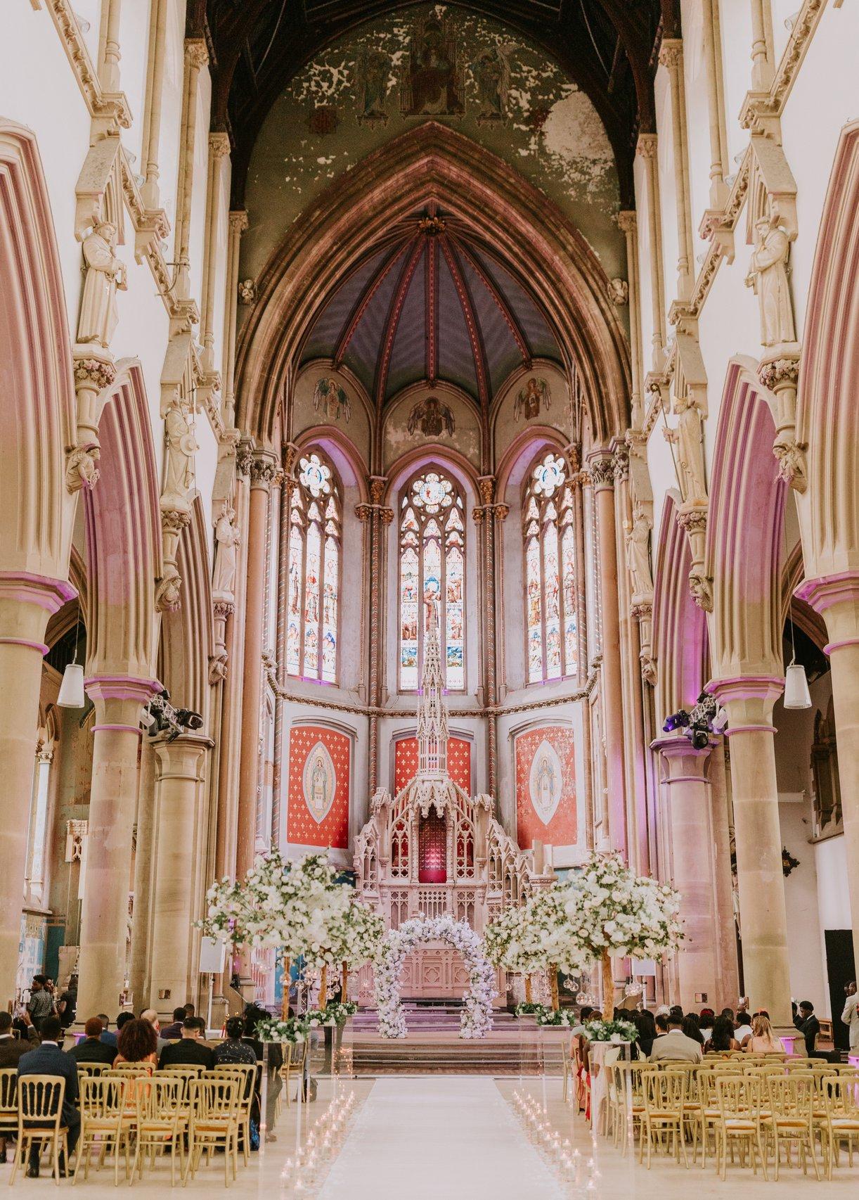 Interior of a Cathedral-like monastery wedding venue set up for a ceremony with chairs facing a grand altar.