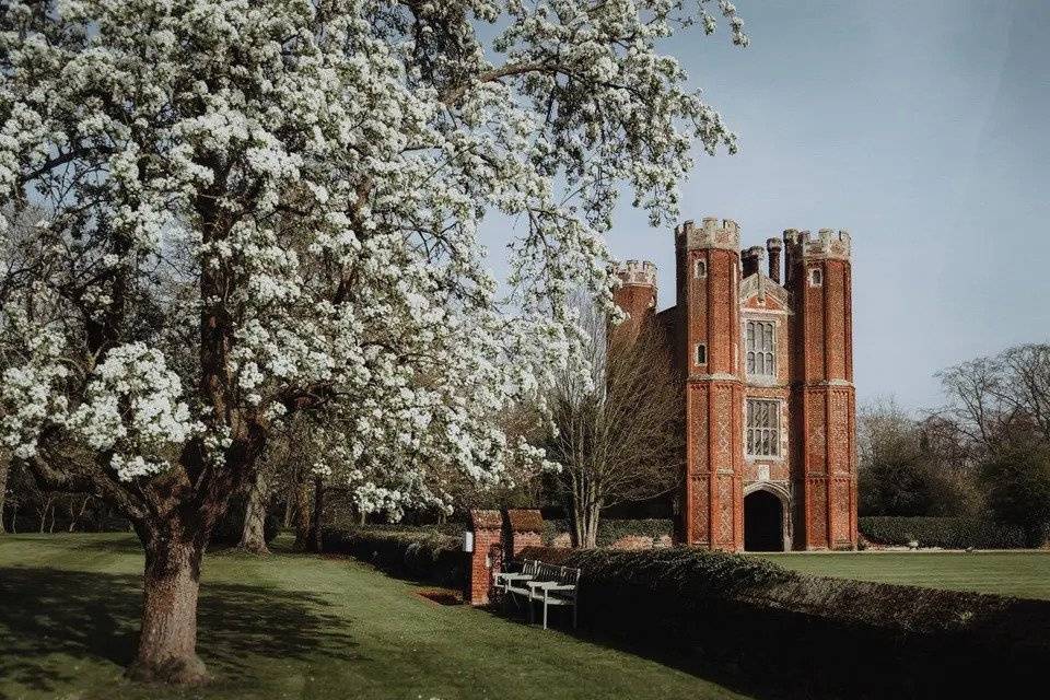 Red brick country wedding venue with green grounds, a blossoming tree and benches