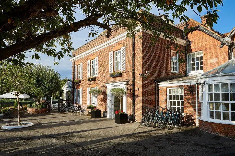 Red brick hotel wedding venue framed by trees with a driveway, garden, outdoor furniture and a bike rack