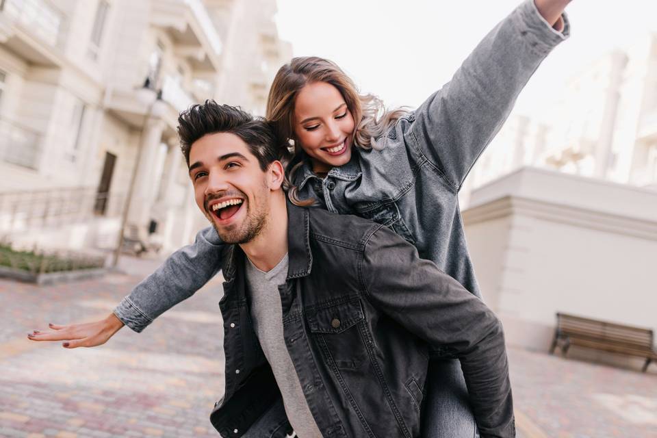 A man giving a woman a piggy back, they are both laughing and smiling.