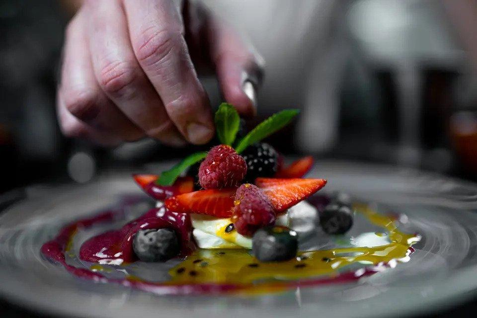 An outstretched hand adjusts the garnish on a dessert topped with fresh berries