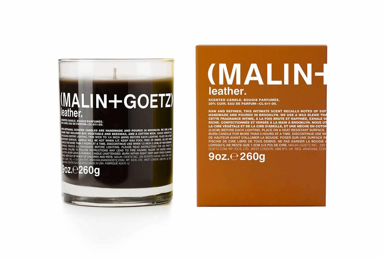 A dark brown candle in a clear glass holder next to its brown packaging which reads 