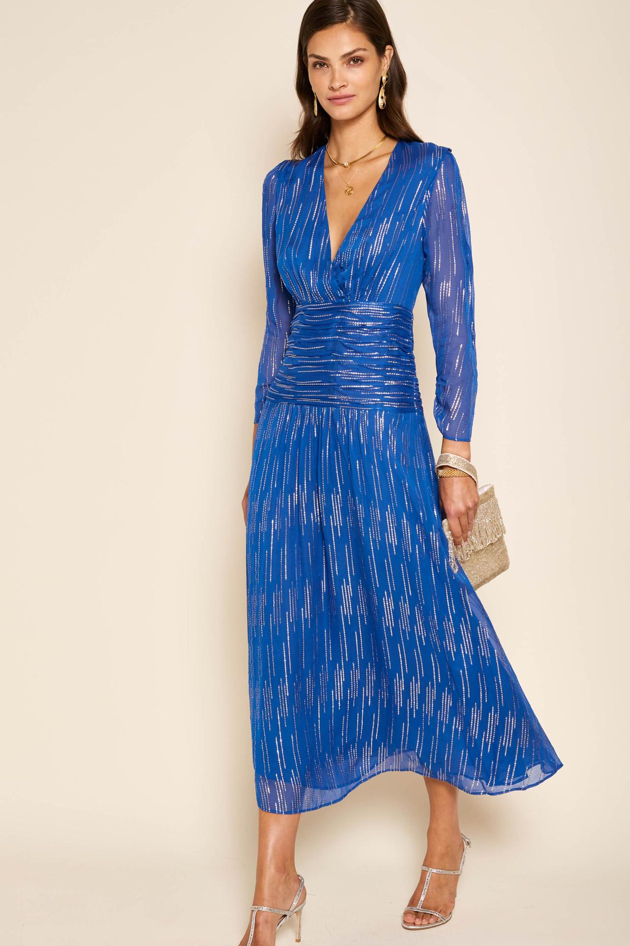 A wedding guest wearing a cobalt blue midi dress with long sleeves. It's flecked with gold lurex.