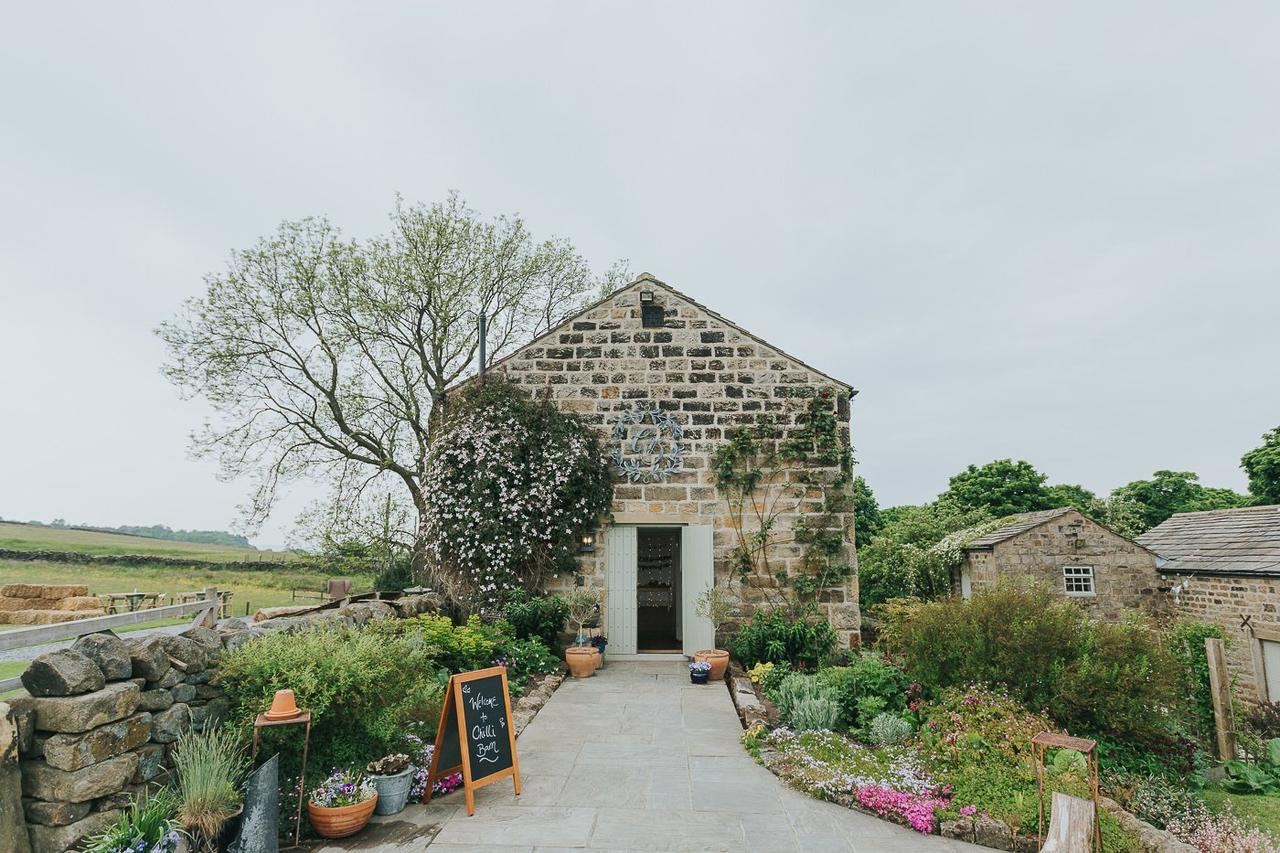 Exterior of a rustic stone barn wedding venue surrounded by fields and pretty gardens.