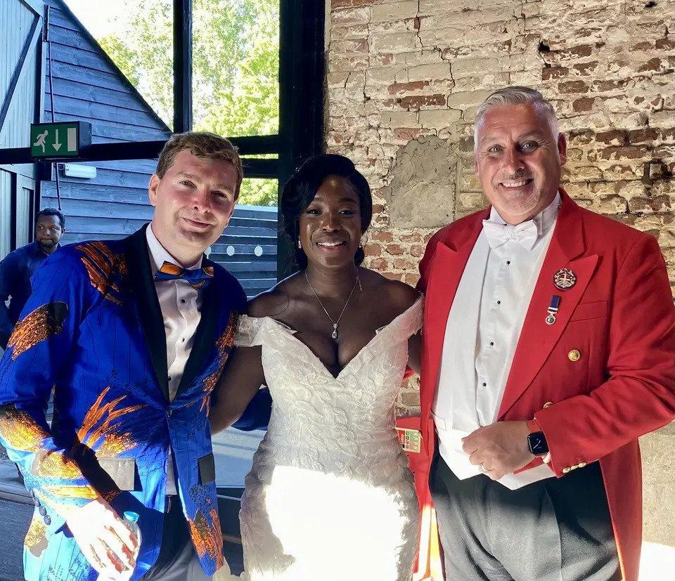 Toastmaster wearing the traditional red jacket next to a bride and a groom wearing a patterned suit