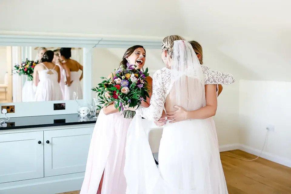 Bride being hugged by two of her bridesmaids on the morning of her wedding in the wedding suite