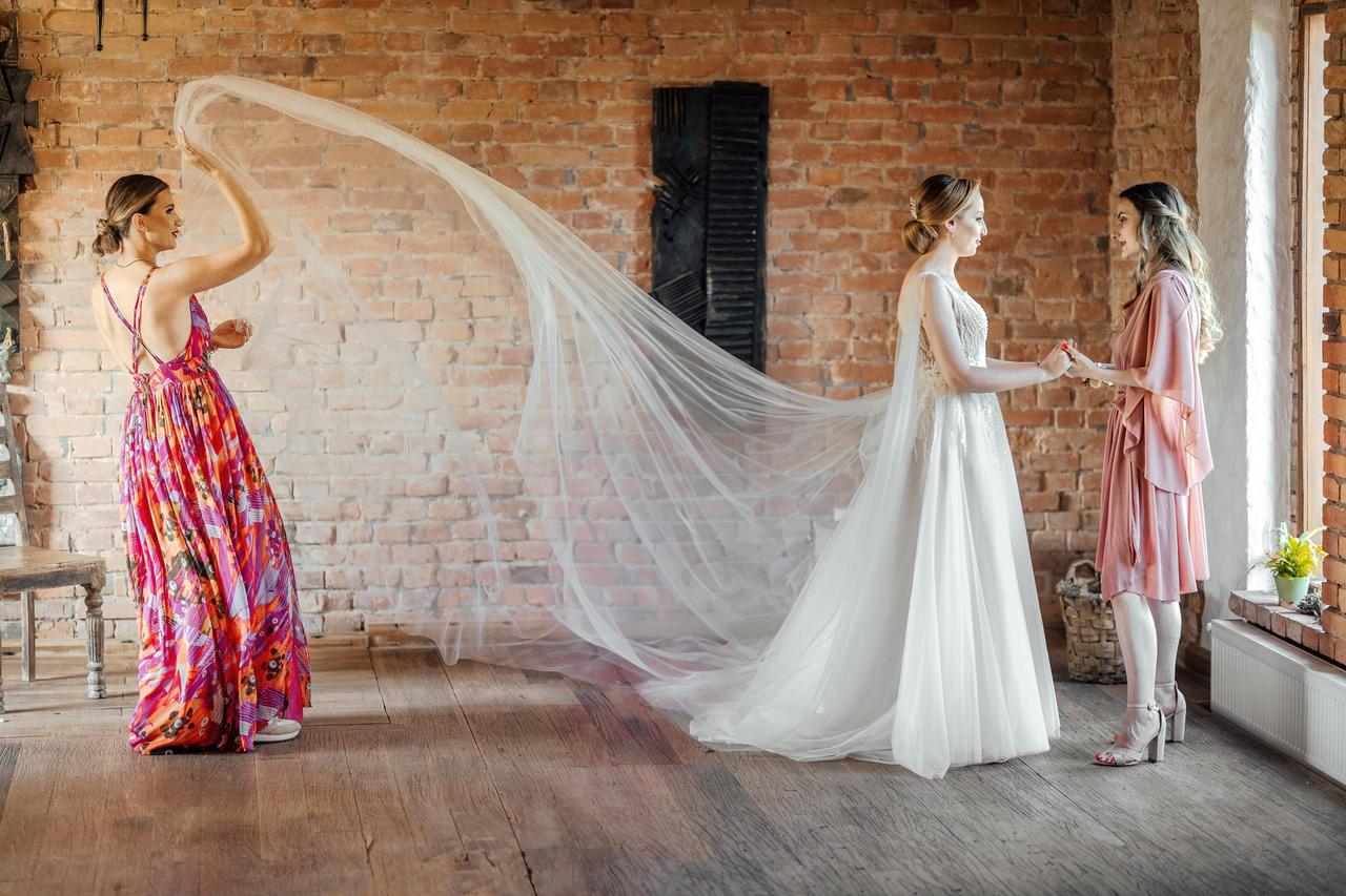 A bride having a serious conversation with a bridesmaid while another one shakes out her veil