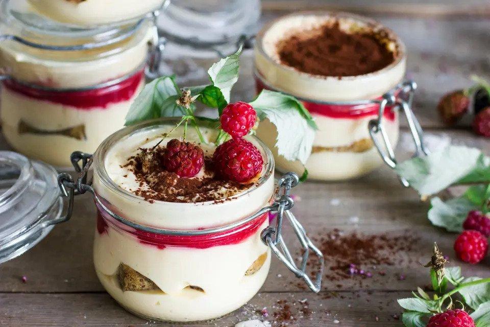 White creamy desserts in mini Mason jars topped with chocolate and fresh berries