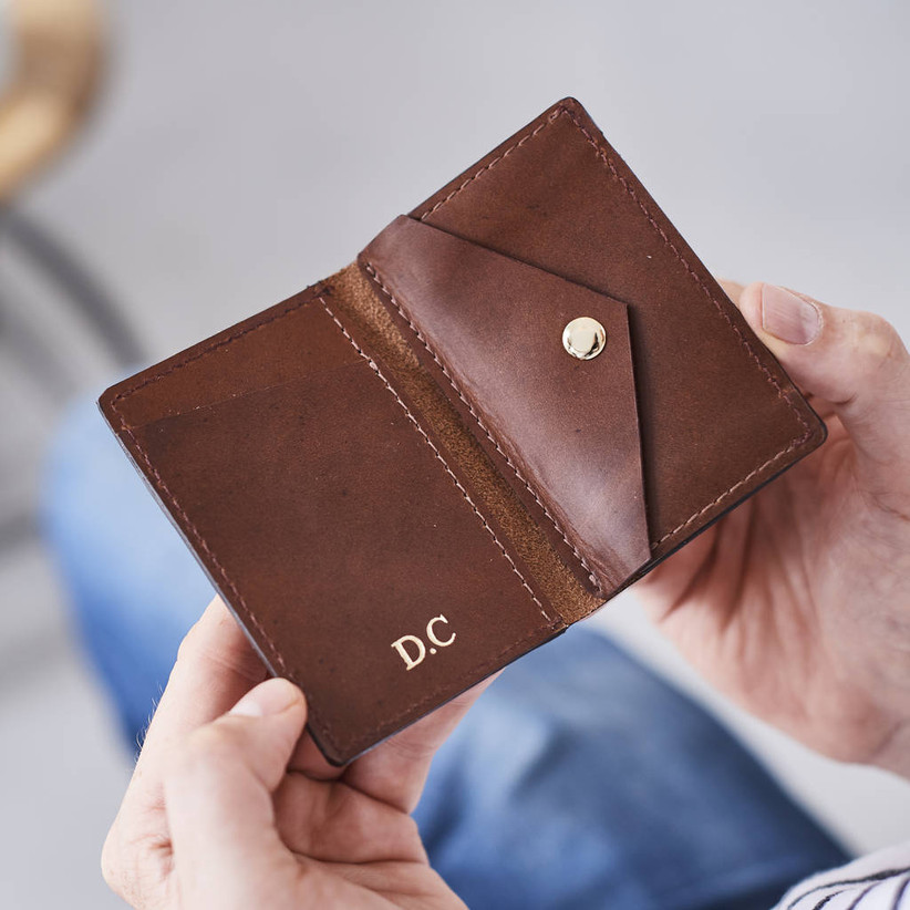 Man opening a brown leather card holder embossed with initials in gold