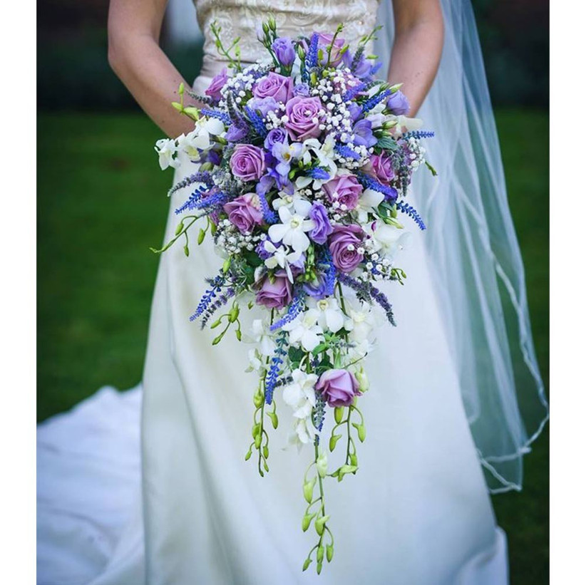 The Most Incredible Cascading Wedding Bouquets Hitched Co Uk Striking purple accent flowers are bursting out between ivory roses and sprinkled with delicate baby's breath. cascading wedding bouquets