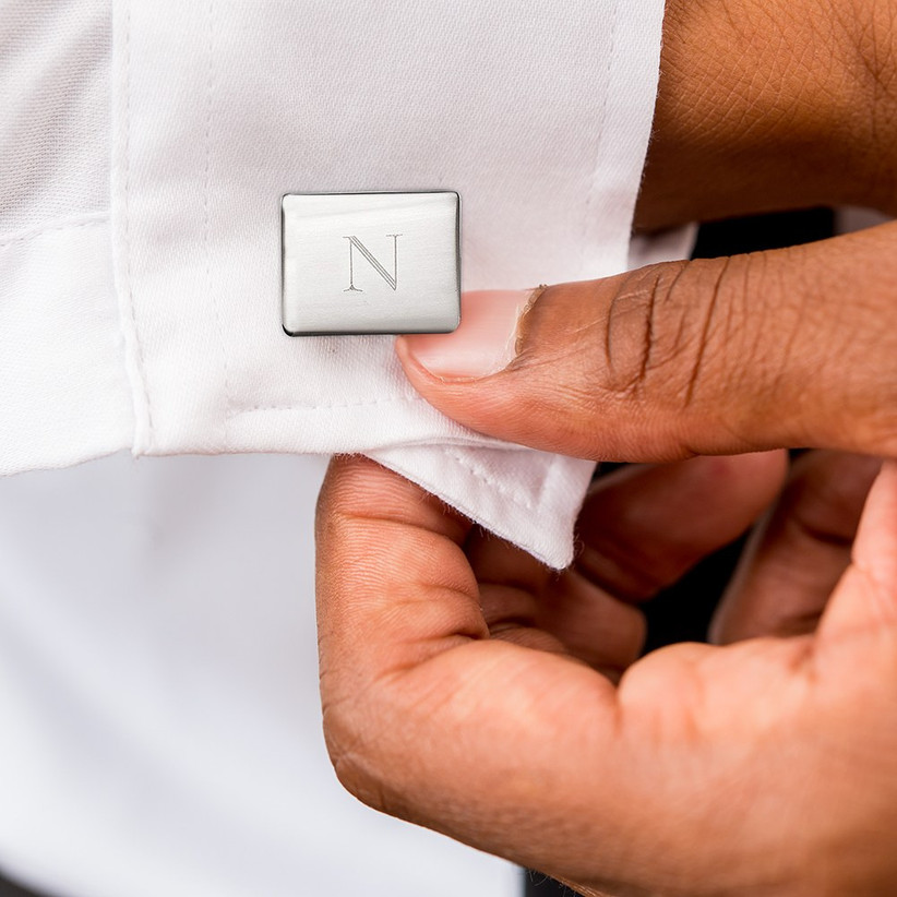 Close up of a man securing a silver monogrammed cuff link onto a white shirt