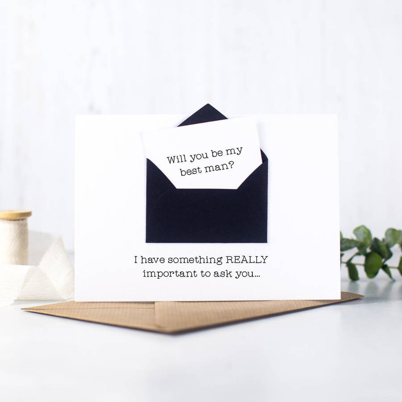 White card with a black envelope on the front containing a note asking will you be my best man
